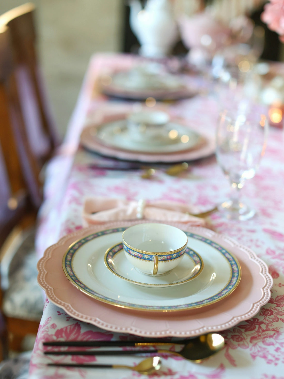 Elegant place setting on a floral, pink tablecloth.