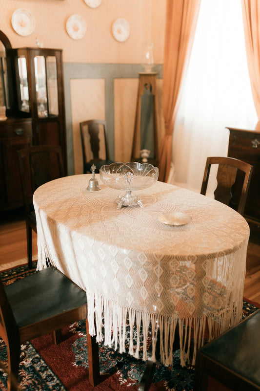 Oval dining table with ornate lace tablecloth and chairs